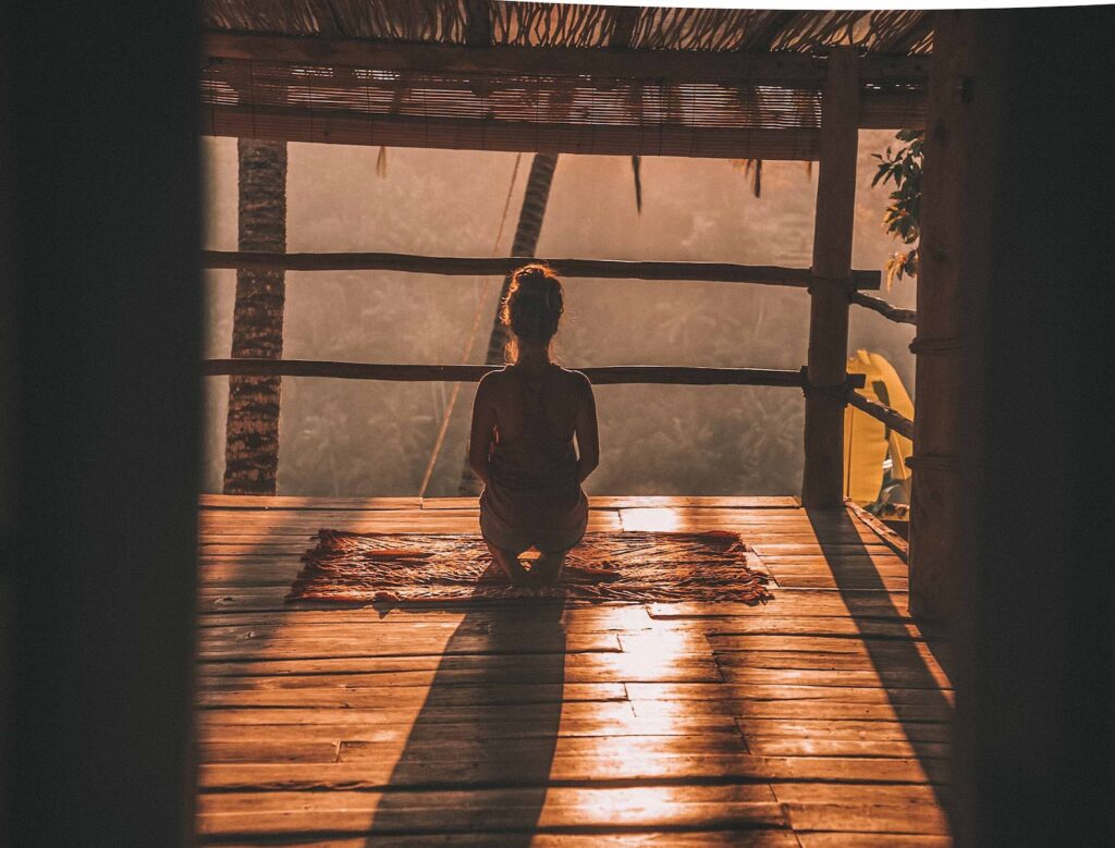 woman meditating on floor with overlooking view of trees